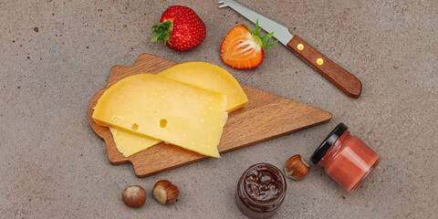 Cheese assortment on wooden boards with strawberries, nuts and jam on stone background