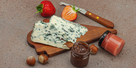 Cheese assortment on wooden boards with strawberries, nuts and jam on stone background