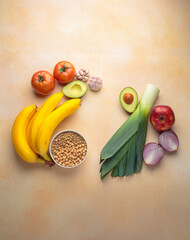 Promoting gut health with prebiotic foods including bananas, lentils, chickpeas, leeks, garlic, tomatoes, avocados, apples, and onions arranged on a textured surface top view