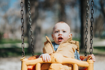A toddler wearing a yellow vest happily plays on a swing in an outdoor park, showcasing the joy of...