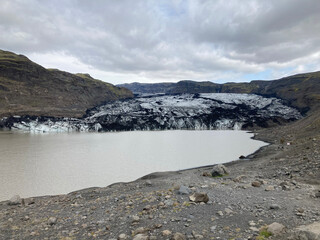 Sólheimajökull Glacier under a gloomy sky, with meltwater in the foreground and jagged ice...
