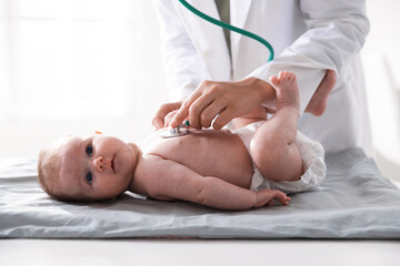 Pediatrician examining baby with stethoscope at table in clinic, closeup