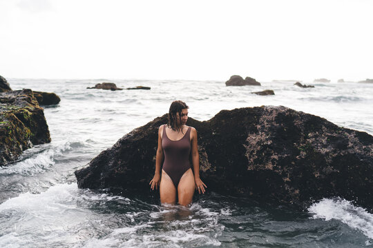 Confident woman stands in shallow water, facing camera with assertive gaze, communicating power, grounded self-image and a rejection of filtered, always-on digital culture.