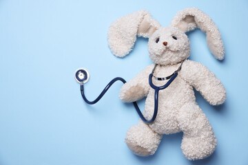 Pediatrics concept. Toy bunny with stethoscope on light blue background, top view. Space for text