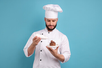 Happy confectioner in uniform holding chocolate dessert and bottle of sauce on light blue background
