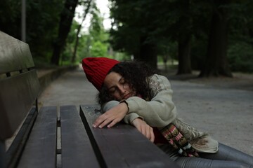 Homeless woman sleeping near bench in park