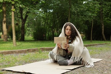 Homeless woman with sign Help and paper cup on carton in park, space for text