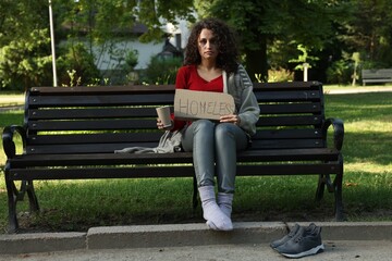 Poor woman with sign Homeless and paper cup on bench in park