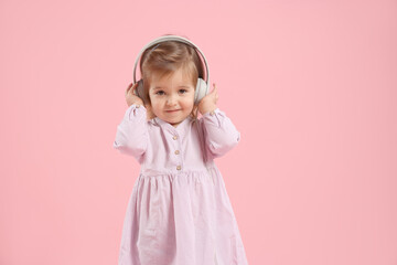 Cute little girl in headphones on pink background