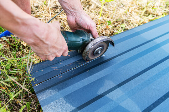 A person is actively cutting a dark grey corrugated metal sheet outdoors with an angle grinder.