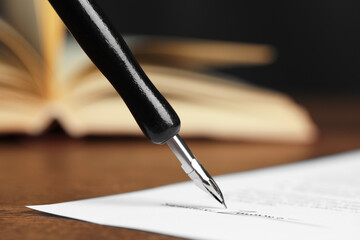 Signing notary document with fountain pen at wooden table against black background, closeup