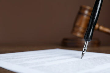 Signing notary document with fountain pen at table against brown background, closeup