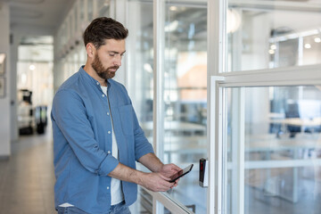 A man uses a smartphone to unlock a door with a biometric scanner, showcasing modern security...
