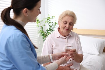 Nurse giving glass of water to senior woman indoors, selective focus. Home health care service