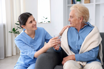 Nurse giving glass of water to senior woman indoors. Home health care service