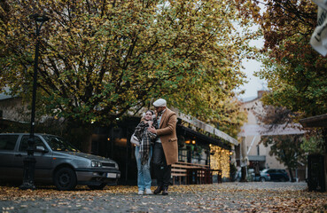 Obraz premium A young couple takes a leisurely walk under colorful autumn trees in an urban setting. The scene captures the essence of romance and tranquility in a bustling city atmosphere.