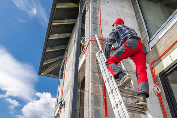 Worker Climbs Ladder to Inspect Construction Site Under Blue Sky With White Clouds