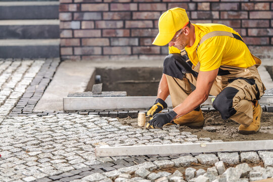 Skilled Worker Laying Cobblestones on a Walkway at a Construction Site During Day