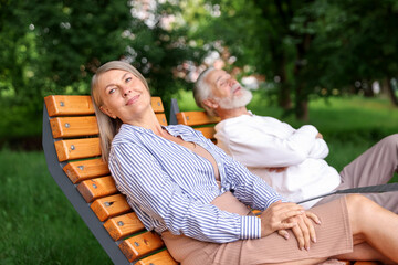 Lovely senior couple resting on wooden sunbeds in park
