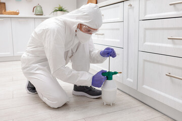 Pest control worker in protective suit spraying insecticide at home