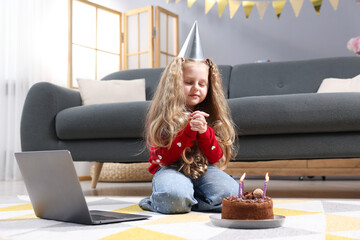 Birthday celebration. Little girl with cake having video call via laptop at home