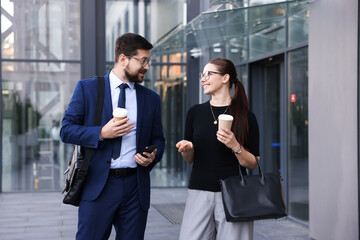 Happy coworkers with coffee discussing something near office building