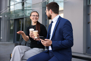 Happy coworkers with smartphone and coffee discussing something near office building