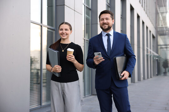 Happy coworkers with smartphone and coffee discussing something near office building - Powered by Adobe