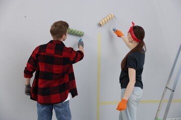 Couple painting wall with rollers in room, back view