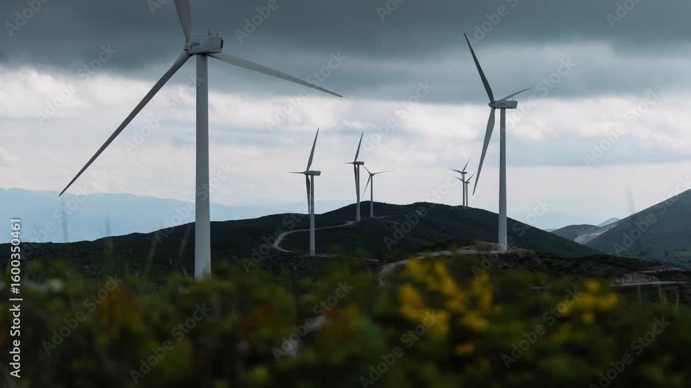 Aufkleber wind turbines on a mountain rapidly rotate beneath a cloudy sky with vibrant bokeh flowers in front 