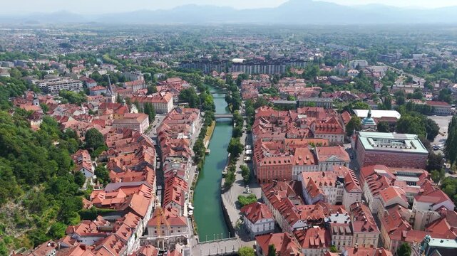 Forward-moving aerial shot glides above Ljubljana&rsquo;s historic core, highlighting Jože Plečnik's distinctive red-brick National University Library NUK next to Ljubljanica River, terracotta rooftops