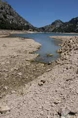 Dried reservoir landscape in a mountainous region under clear blue sky, showing dramatically low...