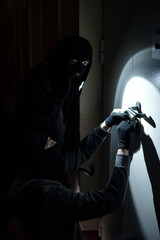 Two men wearing black hooded clothing and gloves breaking into locked door with flashlight and...