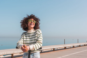 Happy Afro woman with electric scooter in seaport enjoying sustainable transport on sunny day