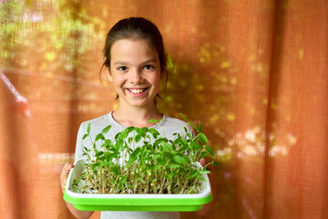 Smiling White girl holding tray of mung bean microgreens at home. Concept of healthy eating, indoor gardening, and eco education for kids