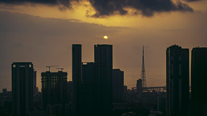 Aerial cinematic image of Mumbai during the monsoon season, featuring dramatic clouds and a glowing sunset over the city skyline. Ideal for themes like residential buildings, and urban cityscapes.