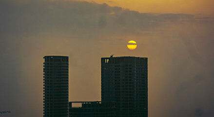 Aerial cinematic image of Mumbai during the monsoon season, featuring dramatic clouds and a glowing sunset over the city skyline. Ideal for themes like residential buildings, and urban cityscapes.