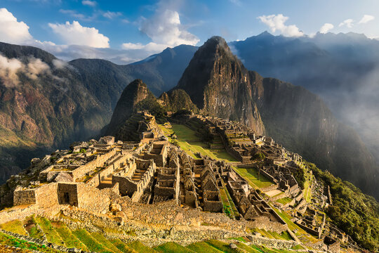 Aerial view of the ancient stone ruins of Machu Picchu, nestled high in the Andes Mountains, shrouded in mist and bathed in the golden light of the sun, Cusco, Peru.