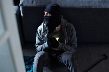 Masked man wearing black balaclava and gloves crouching on floor holding flashlight looking to side...