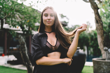 Serene woman poses outdoors in natural sunlight, softly holding hair—symbol of inner calm,...