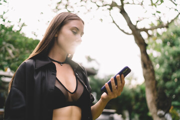 Close-up of young woman using smartphone outdoors with focused look—tech-savvy digital nomad...