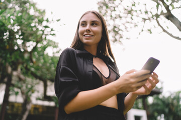 Woman standing barefoot in lush garden with smartphone, smiling softly—moment of connection,...