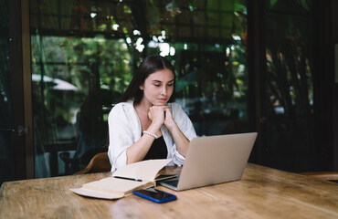 Freelancer woman rests hands under chin while focusing on laptop screen, surrounded by...