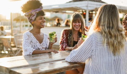 Happy multiracial girls drinking mojitos on the beach at sunset party - Summer vacation and people lifestyle concept - Main focus on left african female face