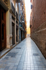 Narrow street in Valencia, featuring charming buildings, cobblestone pavement, and warm natural light inviting exploration at dawn. Ideal for travel and architecture themes.