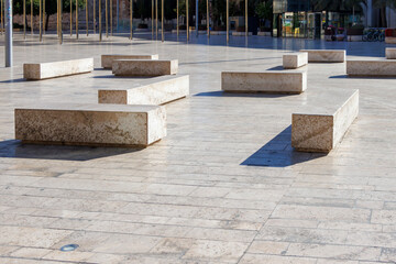 Obraz premium Modern benches arranged on the plaza in Plaza de la Virgen, Valencia. Sunlight casts shadows, highlighting the architecture and vibrant atmosphere of the public space.