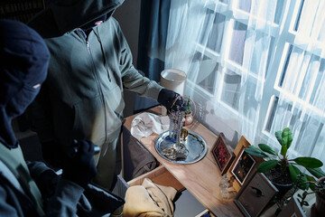Two men wearing hooded sweatshirts and gloves stealing jewelry and valuables from bedroom dresser...