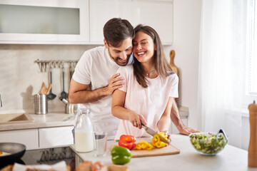 Happy couple engaged in cooking as they chop colorful vegetables in a modern kitchen, creating an atmosphere of joy and teamwork during a sunny day.