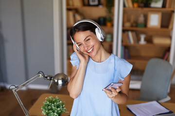 A person in a home office listens to music through headphones, smiling happily while holding a...