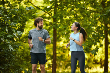 Two people are jogging together in a vibrant park filled with tall trees, celebrating fitness and...